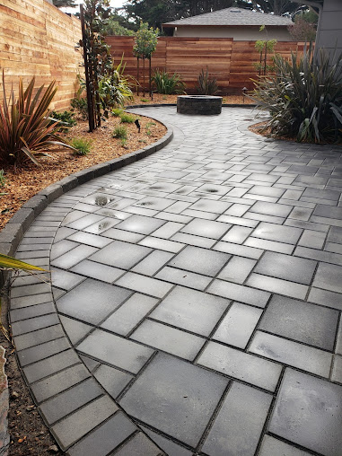 Finished curved paver path leading to a backyard fire pit